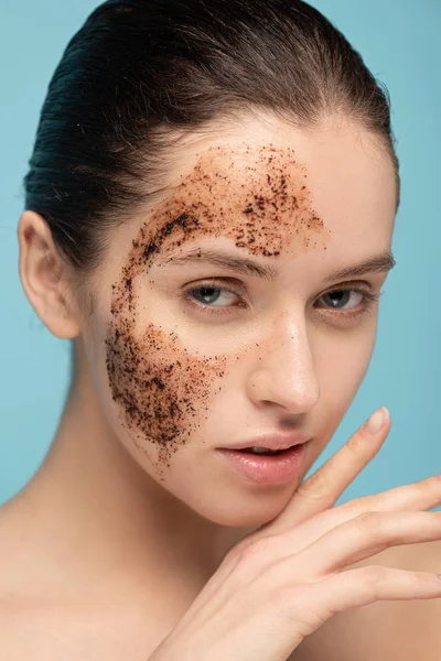 Junge Frau schrubbt Kaffee im Gesicht, isoliert auf blauem Grund — Stockfoto