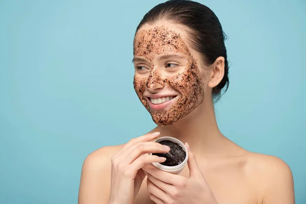 Ragazza positiva applicare scrub caffè dal contenitore di plastica, isolato su blu — Foto stock