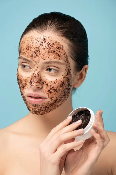 Schöne Mädchen Anwendung Kaffee-Peeling aus Kunststoff-Container, isoliert auf blau — Stockfoto