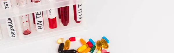 Панорамний знімок пробних трубок із зразками крові та плямистою плямою біля таблеток ізольовано на білому — стокове фото