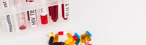 Panoramic shot of test tubes with blood samples and lettering near pills isolated on white — Stock Photo