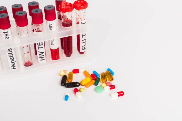 Test tubes with blood samples and lettering near pills isolated on white — Stock Photo