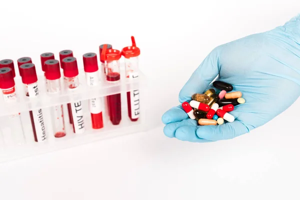 Vista recortada de científico en guantes de látex sosteniendo pastillas cerca de tubos de ensayo con letras aisladas en blanco - foto de stock