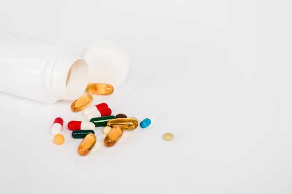 Garrafa perto de pílulas coloridas isoladas em branco com espaço de cópia — Fotografia de Stock