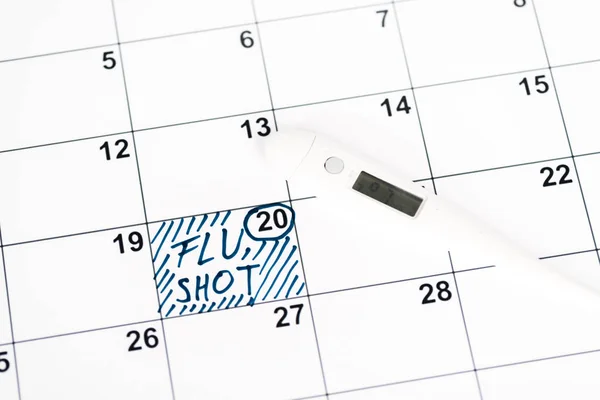 Digital thermometer on calendar with marked date and flu shot lettering — Stock Photo