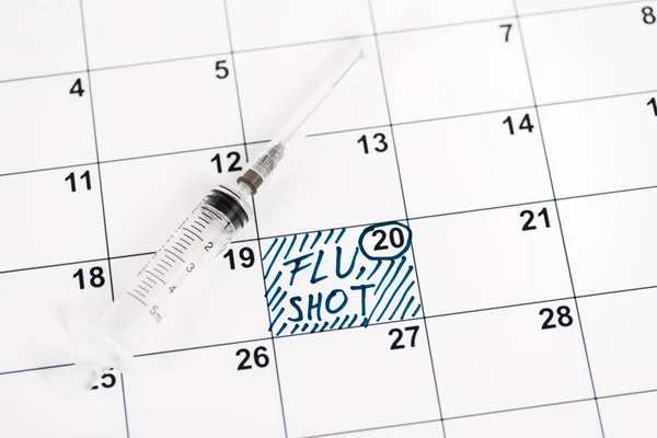 Jeringa en el calendario con fecha marcada y letras de la vacuna contra la gripe - foto de stock