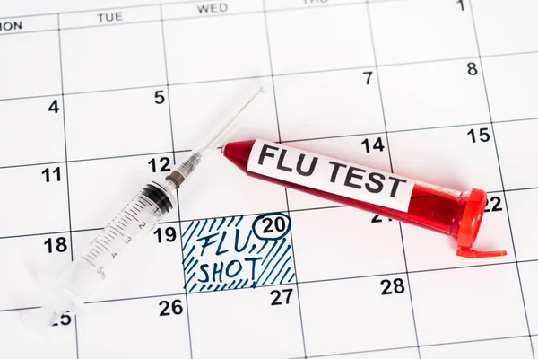 Campione con test influenzale vicino alla siringa sul calendario con data segnata e iscrizione per iniezione influenzale — Foto stock