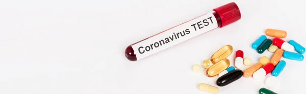 Panoramic shot of colorful pills near sample with coronavirus test lettering isolated on white — Stock Photo