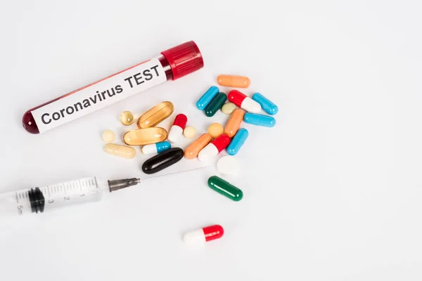 Барвисті таблетки поблизу зразка з коронавірусною пробкою та шприцом на білому — стокове фото
