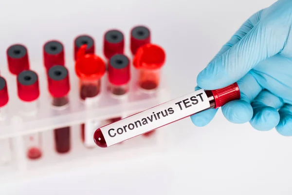 Selective focus of scientist holding sample with coronavirus test lettering near test tubes isolated on white — Stock Photo