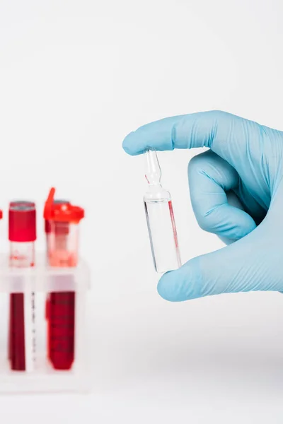 Vista recortada del científico sosteniendo botella de vidrio con líquido cerca de tubos de ensayo en blanco - foto de stock