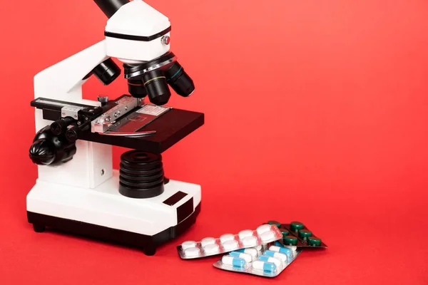 Microscope near pills in blister packs on red — Stock Photo