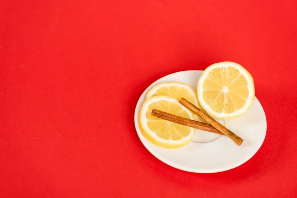 Limoni affettati su piattino con bastoncini di cannella su rosso — Foto stock