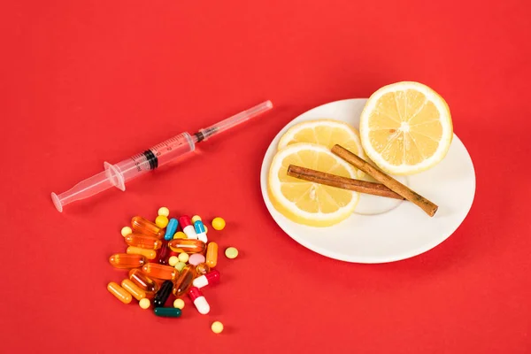Syringe near sliced lemons, cinnamon sticks and pills on red — Stock Photo
