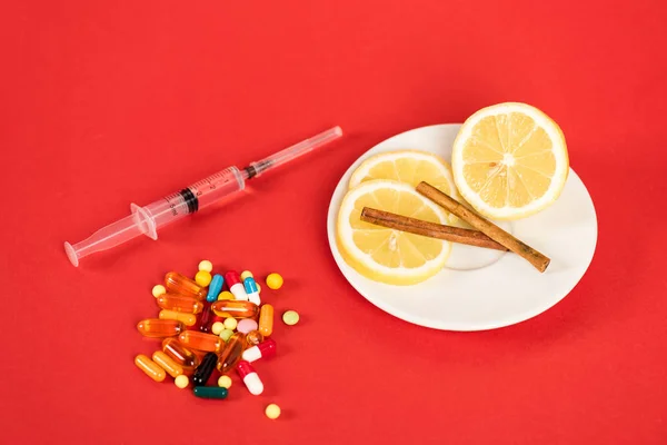 Syringe near sliced lemons, cinnamon sticks and pills on red — Stock Photo