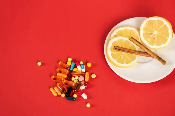 Top view of sliced lemons and cinnamon sticks near pills on red — Stock Photo