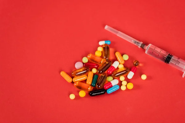 Top view of colorful pills near syringe on red with copy space — Stock Photo