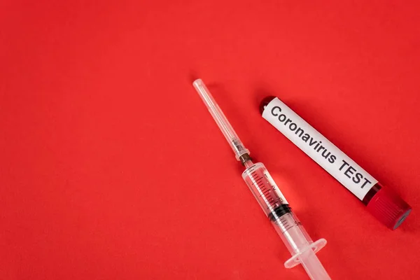 Top view of sample with coronavirus test lettering near syringe on red — Stock Photo