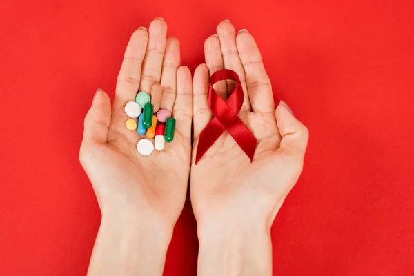 Vista dall'alto della donna che tiene il nastro rosso come consapevolezza hiv e pillole sul rosso — Foto stock