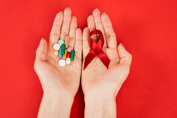 Top view of woman holding red ribbon as hiv awareness and pills on red — Stock Photo