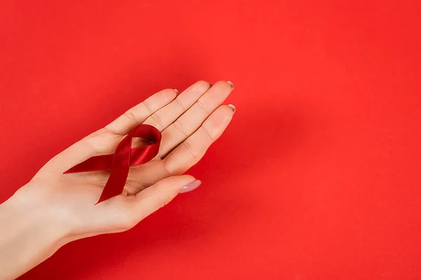 Vista recortada de la mujer sosteniendo cinta roja como conciencia de la colmena en rojo - foto de stock