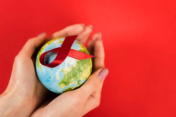 Cropped view of woman holding globe with red ribbon as hiv awareness isolated on red — Stock Photo