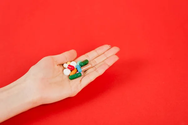 Cropped view of woman holding colorful pills on red — Stock Photo