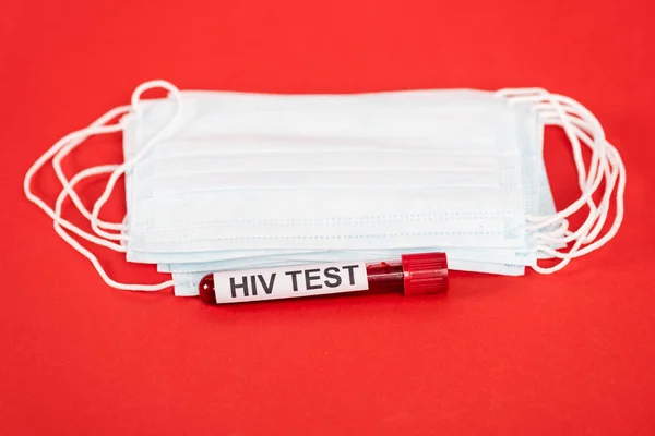 Amostra com letras de teste hiv perto de máscaras médicas protetoras isoladas em vermelho — Fotografia de Stock