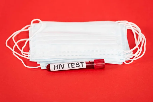 Muestra con letras de prueba hiv cerca de máscaras médicas protectoras aisladas en rojo - foto de stock