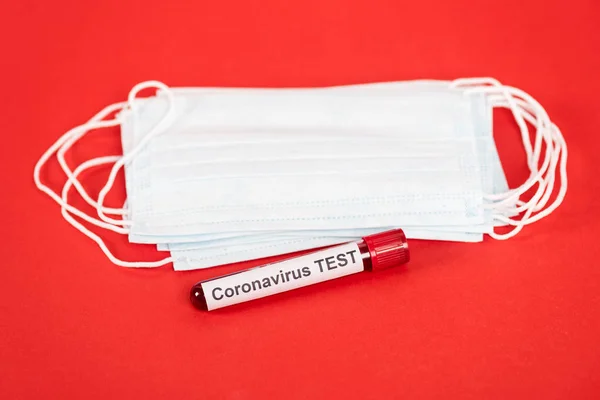 Muestra con letras de prueba de coronavirus cerca de máscaras médicas protectoras aisladas en rojo - foto de stock