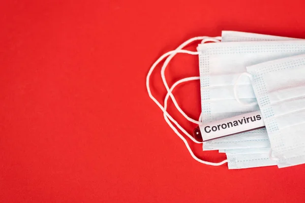 Top view of sample with coronavirus lettering near protective medical masks on red — Stock Photo