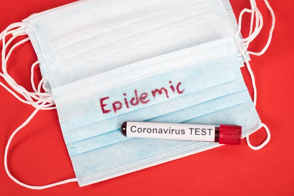 Draufsicht der Probe mit Coronavirus-Test in der Nähe medizinischer Schutzmasken mit Epidemie-Schriftzug auf Rot — Stockfoto