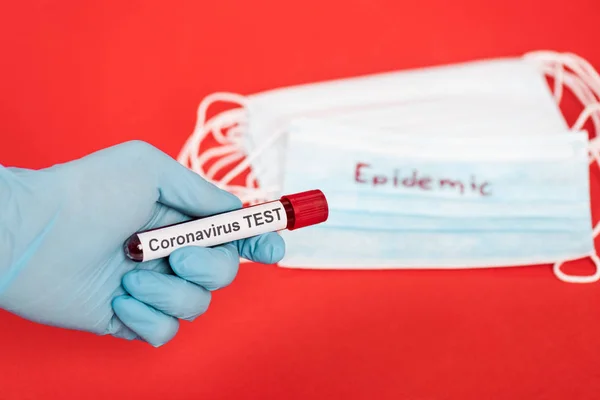 Обрезанный вид ученого, держащего образец с коронавирусной надписью рядом с медицинскими масками, изолированными на красном — стоковое фото