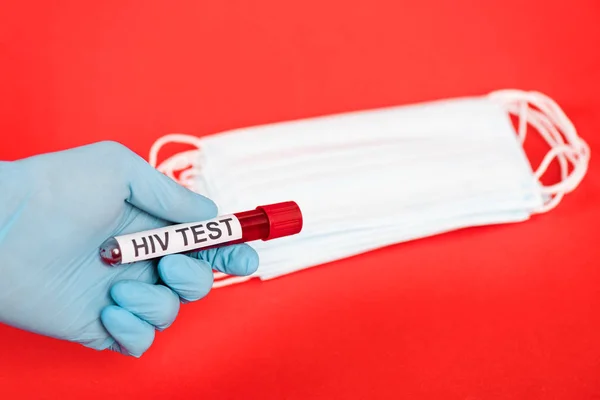 Abgeschnittene Ansicht eines Wissenschaftlers, der eine Probe mit Hiv-Test-Schriftzug in der Nähe medizinischer Masken auf Rot isoliert hält — Stockfoto