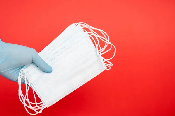 Vista recortada del científico sosteniendo máscaras médicas aisladas en rojo - foto de stock