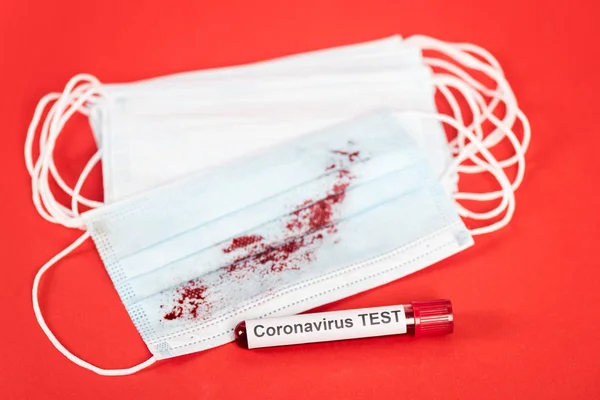 Selective focus of sample with coronavirus test lettering near medical masks with blood on red — Stock Photo