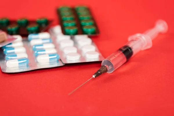 Foco seletivo da seringa perto de pílulas no vermelho — Fotografia de Stock