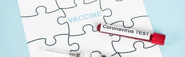 Panoramic shot of puzzle pieces with vaccine lettering near sample with coronavirus test and syringe on blue — Stock Photo