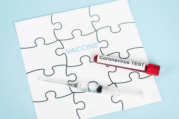 Puzzle pieces with vaccine lettering near sample with coronavirus test and syringe on blue — Stock Photo