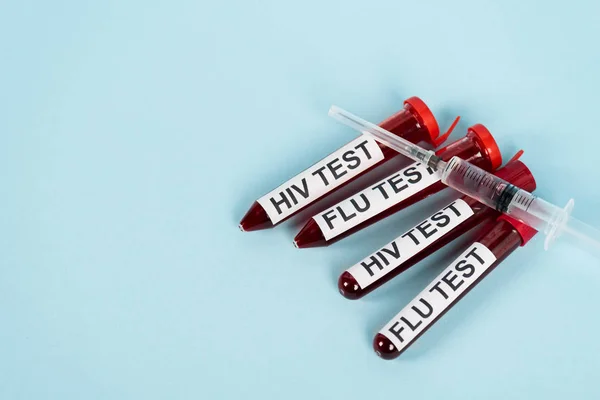 Top view of syringe on samples with hiv test and flu test lettering on blue — Stock Photo