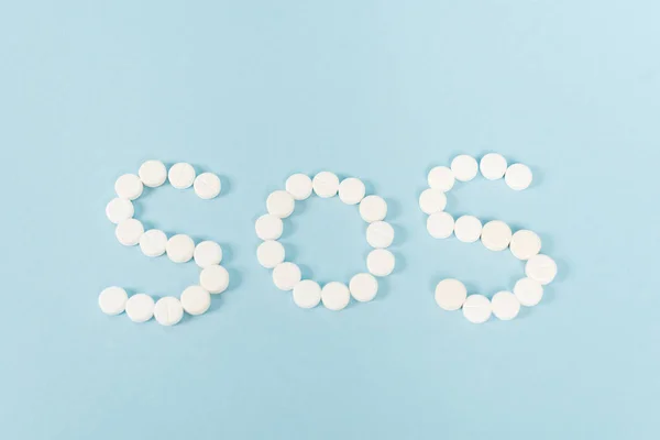 Vista superior de pílulas com letras sos em azul — Fotografia de Stock