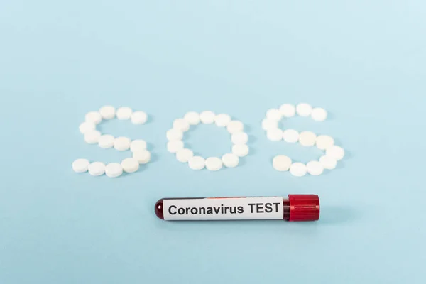 Amostra com teste coronavírus perto de pílulas com letras sos em azul — Fotografia de Stock