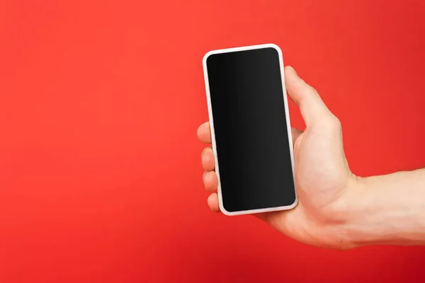 Vista recortada del hombre sosteniendo teléfono inteligente con pantalla en blanco aislado en rojo - foto de stock