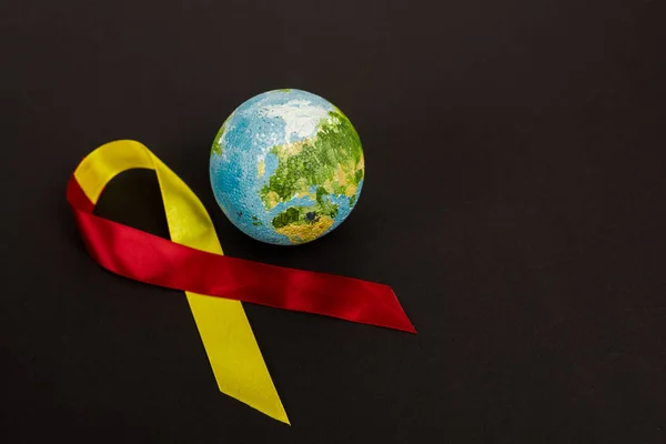 Globe près du ruban rouge et jaune comme sensibilisation à l'hépatite c isolé sur noir — Photo de stock