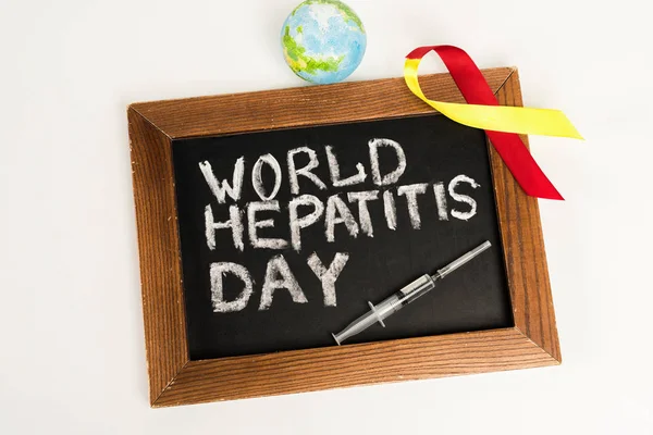 Top view of chalkboard with world hepatitis day lettering near ribbon, globe and syringe isolated on white — Stock Photo