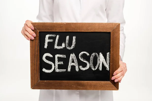 Vista cortada do médico segurando quadro com letras estação da gripe isolado no branco — Fotografia de Stock