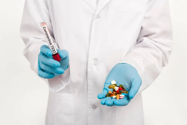 Обрезанный вид ученого, держащего образец с коронавирусной надписью и таблетками, изолированными на белом — стоковое фото