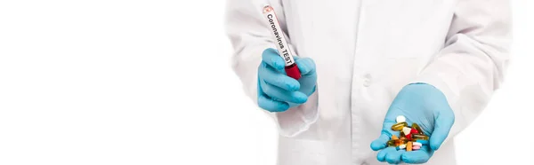 Panoramic shot of scientist holding sample with coronavirus test lettering and pills isolated on white — Stock Photo