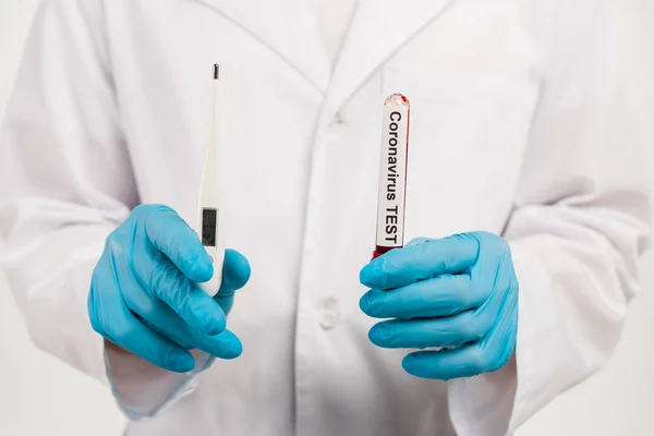 Cropped view of scientist holding sample with coronavirus test lettering and digital thermometer isolated on white — Stock Photo