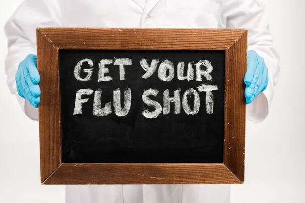 Cropped view of scientist in latex gloves holding chalkboard with get your flu shot lettering isolated on white — Stock Photo